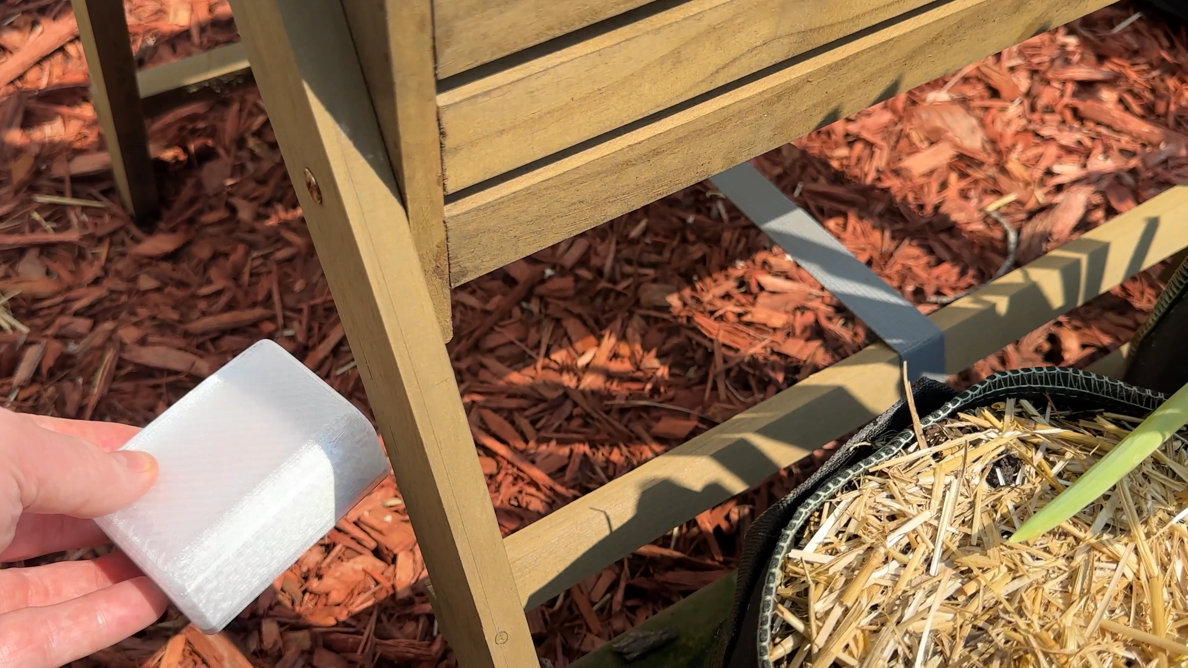 A Bald SENSE sensor enclosure being placed beside a raised garden bed for outdoor testing.